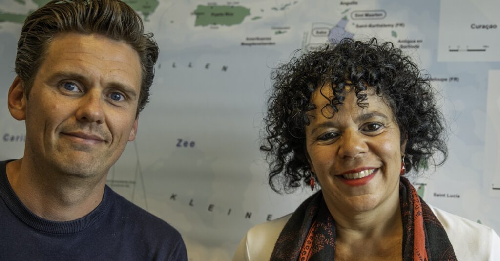 Two smiling adults posing for a photo in front of a world map backdrop.