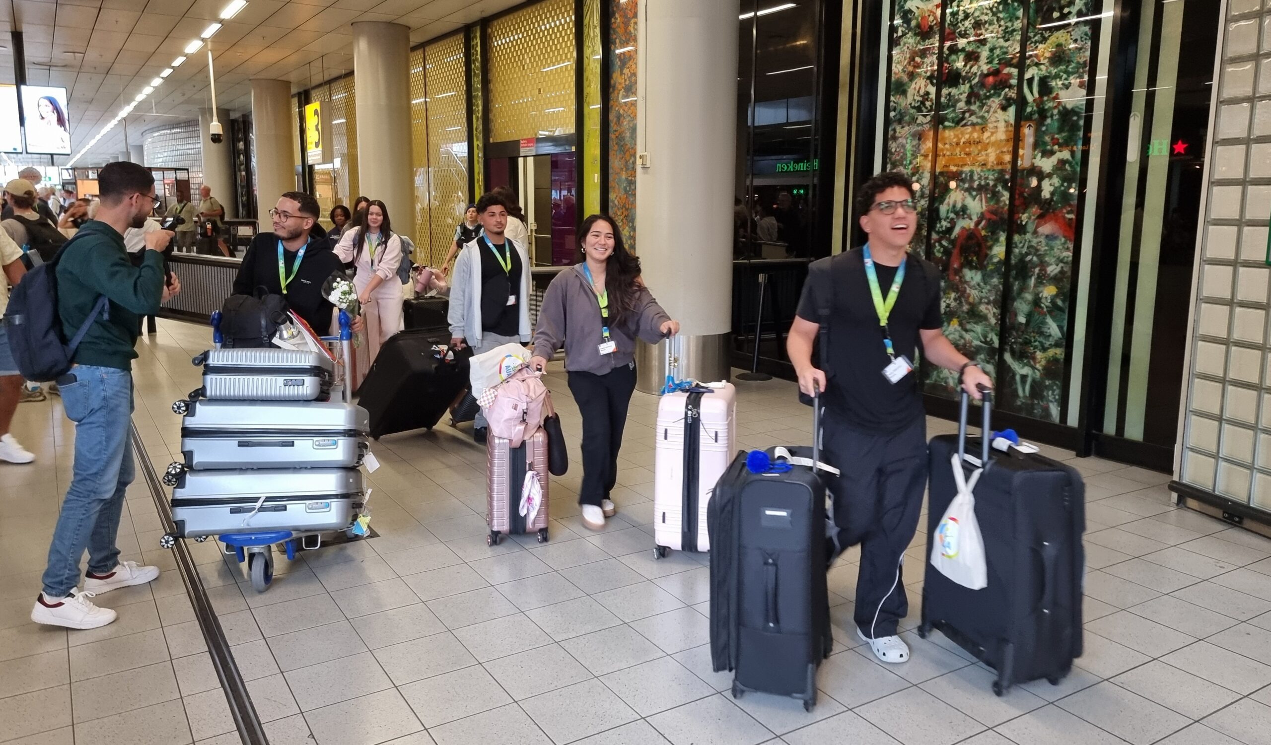 Group of travelers with rolling suitcases and backpacks in an airport terminal, smiling and talking near gate areas.