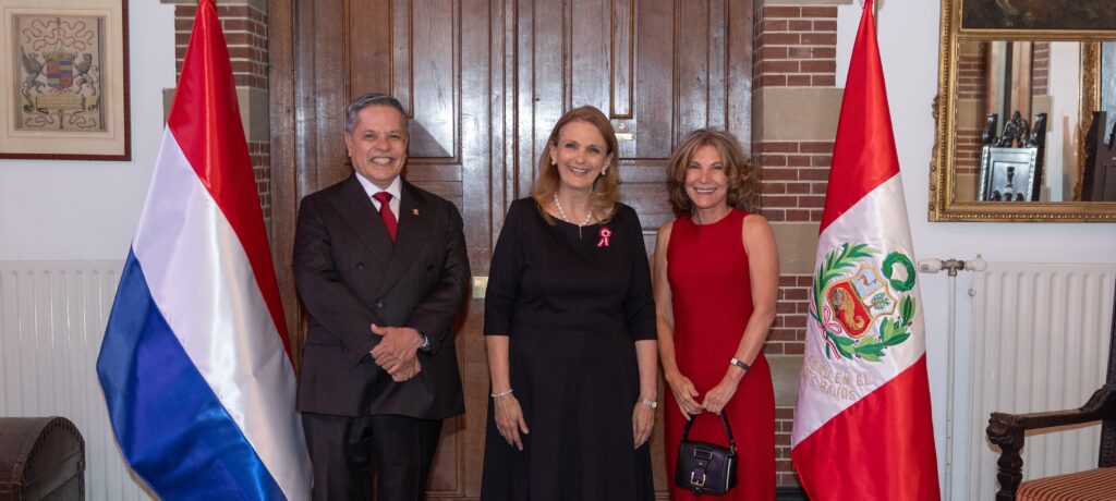 Three adults in formal attire posing for a ceremonial portrait between two national flags in a wood-paneled room.